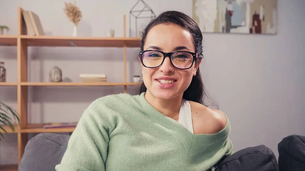 Pretty woman in eyeglasses smiling at camera on couch at home — Stock Photo