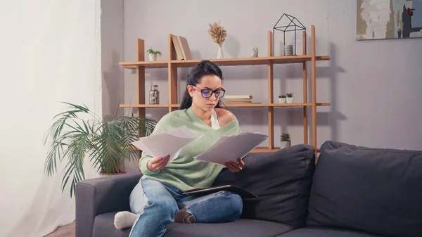 Focused student looking at papers on couch in living room — Stock Photo