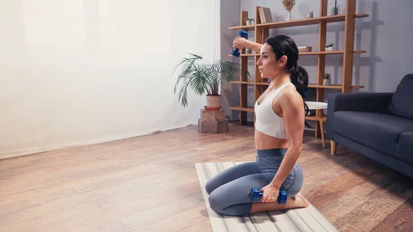 Vue latérale d'une femme sportive faisant de l'exercice avec des haltères dans le salon — Photo de stock