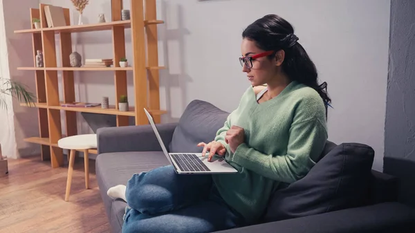 Vista lateral de la mujer en gafas que trabajan en el ordenador portátil en casa - foto de stock
