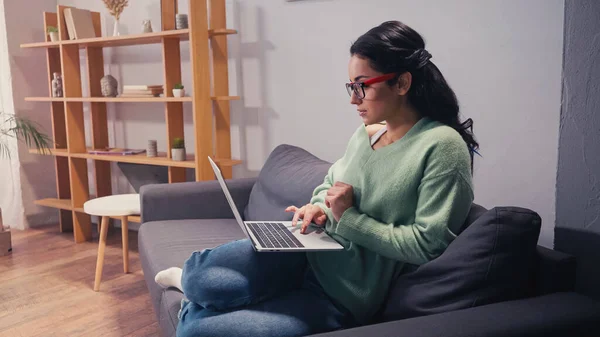 Side view of woman in eyeglasses working on laptop at home — Stock Photo