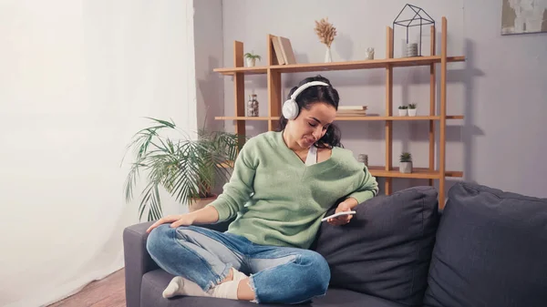 Smiling woman in wireless headphones using smartphone on couch — Stock Photo
