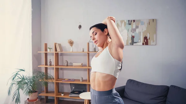 Ziemlich fitte Frau streckt Arme im Wohnzimmer aus — Stockfoto