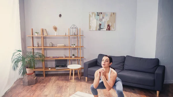 Pretty sportswoman doing squat in living room — Stock Photo