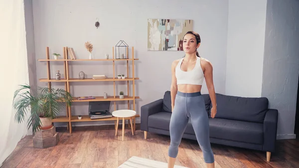 Brünette Frau in Sportbekleidung steht zu Hause auf Fitnessmatte — Stockfoto