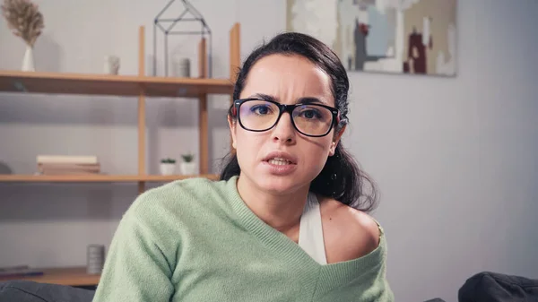Зосереджена жінка в окулярах дивиться на камеру вдома — стокове фото