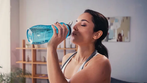 Молода спортсменка п'є воду у вітальні — стокове фото