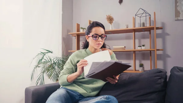 Brünette Studentin mit Brille hält Papiere auf Couch — Stockfoto