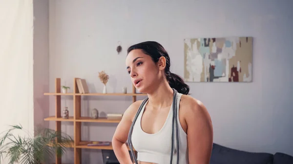 Exhausted sportswoman with jump rope standing in living room — Stock Photo