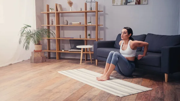 Mujer joven haciendo flexiones de presión cerca de sofá en casa - foto de stock
