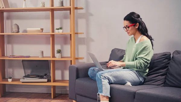 Freelancer in eyeglasses using laptop on couch — Stock Photo