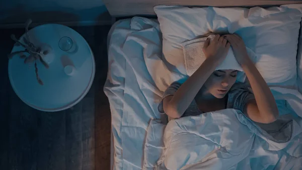 Top view of sick woman with towel on head lying on bed — Stock Photo