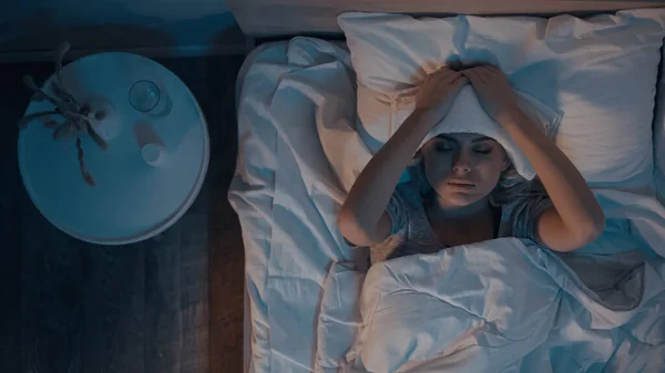 Вид зверху на хвору жінку тримає рушник на голові, лежачи на ліжку — стокове фото