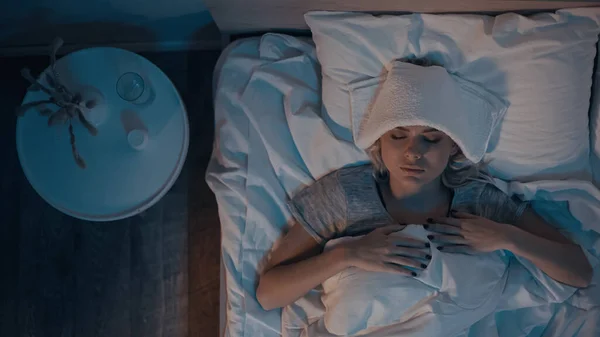 Vue du dessus de la femme malade couchée sur le lit près de l'eau et des pilules dans la chambre — Photo de stock
