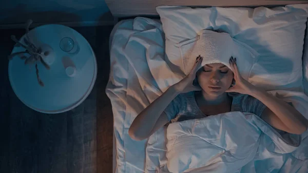 Vista superior de la mujer enferma tocando la cabeza en la cama por la noche - foto de stock