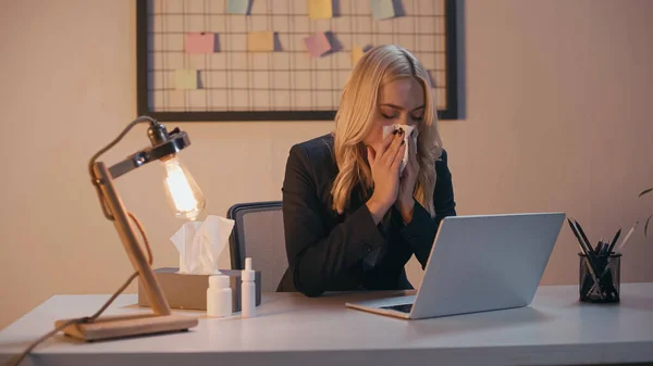 Empresária sofrendo de corrimento nasal perto de pílulas e laptop no escritório — Fotografia de Stock