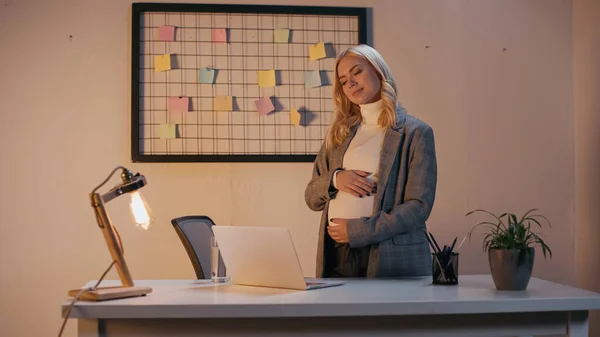 Schwangere Geschäftsfrau schaut abends auf Laptop auf Bürotisch — Stockfoto