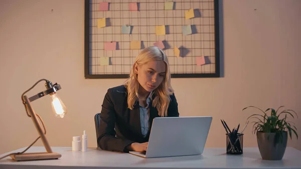 Businesswoman usando el ordenador portátil cerca de píldoras y aerosol nasal en la oficina - foto de stock