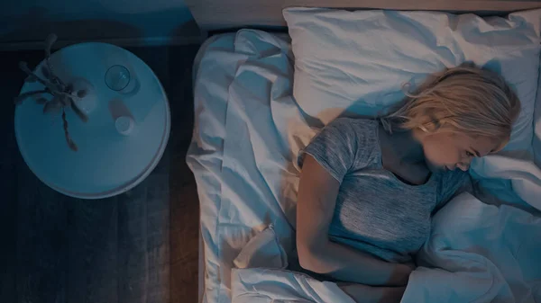 Vue du dessus de la jeune femme couchée sur le lit près des pilules et de l'eau sur la table de chevet — Photo de stock