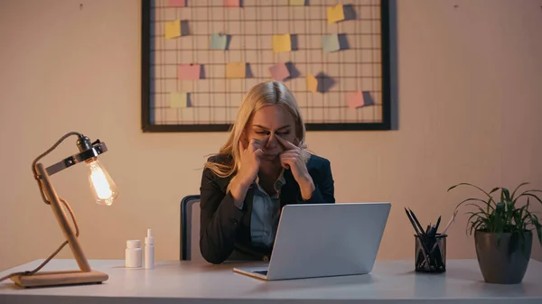 Businesswoman suffering from runny nose near laptop and pills on table in office — Stock Photo