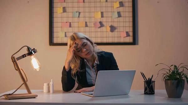 Donna d'affari stanca seduta vicino al computer portatile e pillole in ufficio — Foto stock