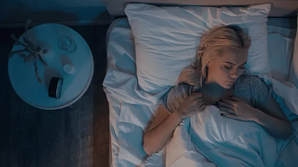 Top view of young woman sleeping near pills and water on bedside table — Stock Photo