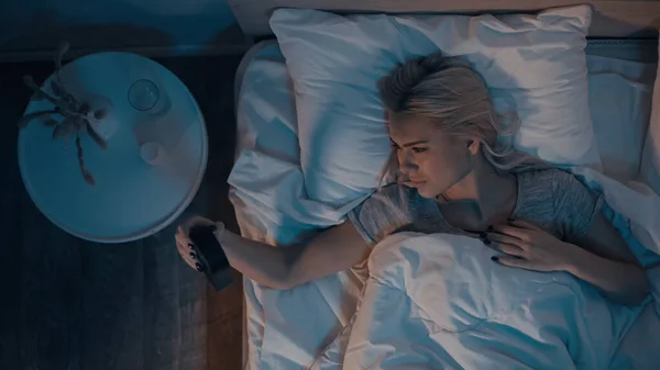 Draufsicht einer Frau, die nachts auf die Uhr schaut, während sie im Bett liegt — Stockfoto
