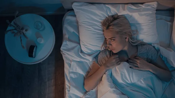 Top view of woman with insomnia looking at alarm clock near pills in bedroom — Stock Photo