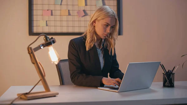 Joven mujer de negocios que usa el ordenador portátil mientras trabaja en la oficina por la noche - foto de stock