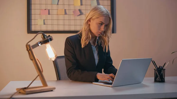 Young businesswoman using laptop while working in office in evening — Stock Photo