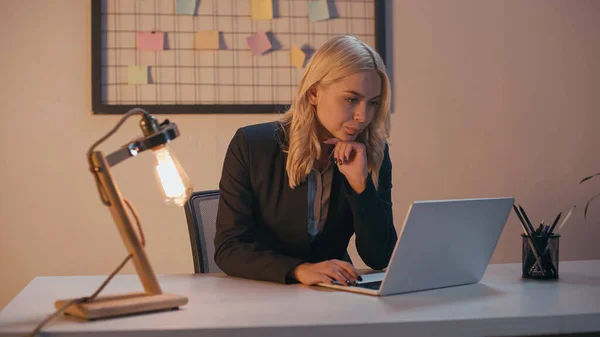 Femme d'affaires travaillant sur ordinateur portable près de la lampe dans le bureau en soirée — Photo de stock