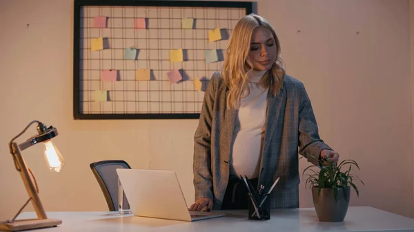 Femme d'affaires enceinte regardant l'usine sur la table de travail dans le bureau — Photo de stock