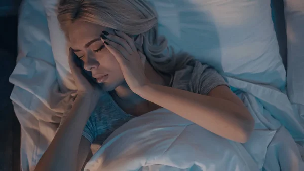 Vue du dessus de la jeune femme avec migraine couchée sur le lit le soir — Photo de stock