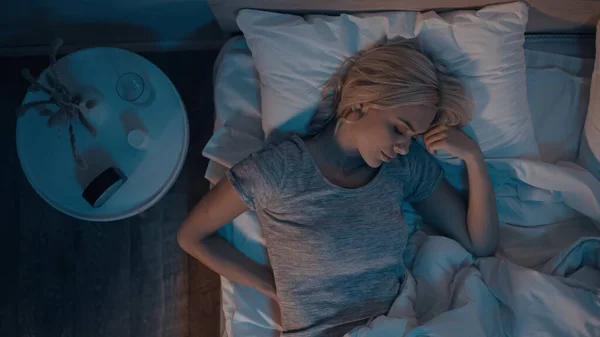 Vue du dessus de la jeune femme dormant sur le lit près des pilules et un verre d'eau sur la table de chevet — Photo de stock