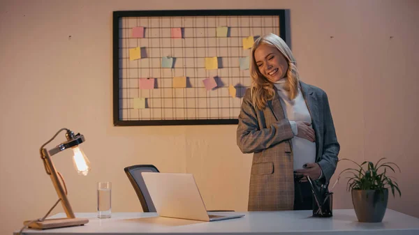 Pregnant businesswoman smiling at laptop during video chat in office — Stock Photo