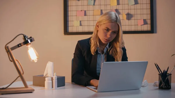 Ill businesswoman using laptop near napkins and nasal spray in office — Stock Photo