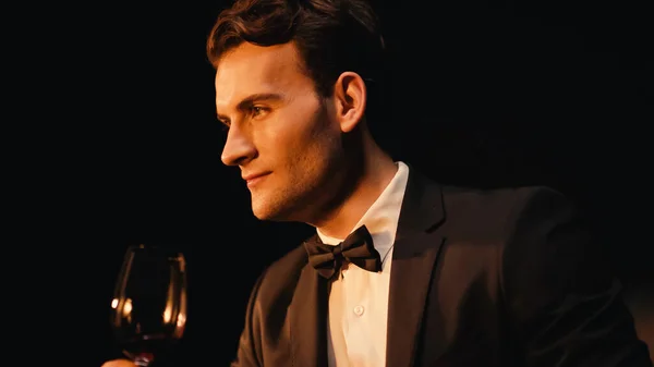 Confident young man in suit holding glass of red wine isolated on black — Stock Photo