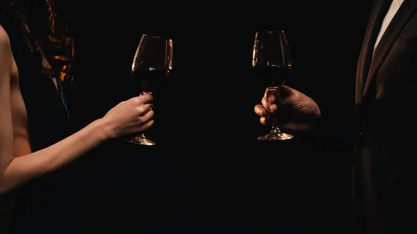 Vista cortada de casal elegante segurando copos com vinho tinto isolado em preto — Fotografia de Stock