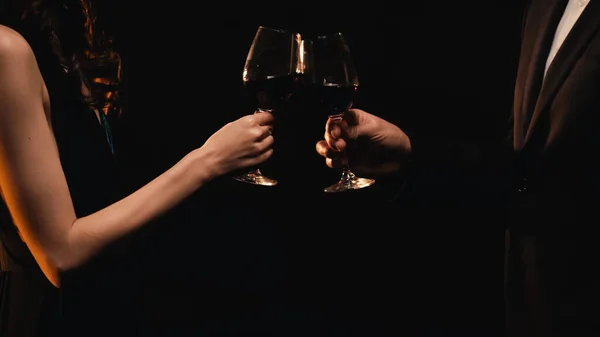 Vista recortada de una elegante pareja de tostadas con copas de vino aisladas en negro - foto de stock