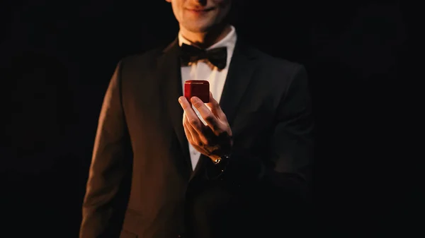 Обрізаний вид людини в костюмі, що тримає червону коробку, роблячи пропозицію ізольованою на чорному — стокове фото