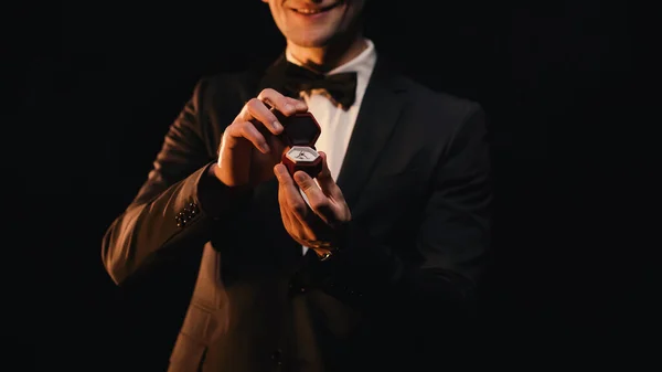 Cropped view of happy man in suit holding red box with wedding ring isolated on black — Stock Photo