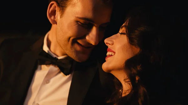 Feliz jovem casal sorrindo e olhando um para o outro isolado no preto — Fotografia de Stock