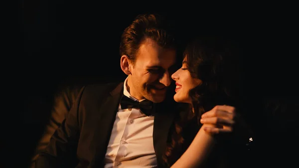 Homme souriant en costume étreignant et flirtant avec petite amie gaie isolé sur noir — Photo de stock