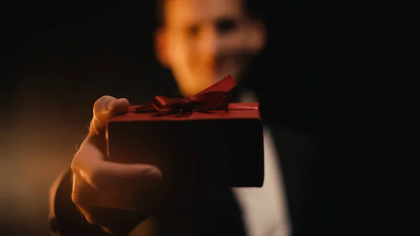 Homme flou en costume montrant boîte cadeau rouge sur noir — Photo de stock