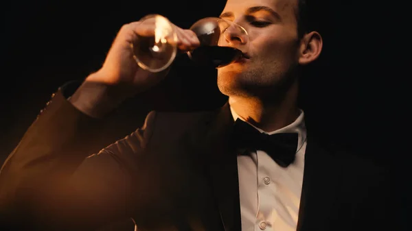 Hombre elegante en traje beber vino tinto aislado en negro - foto de stock