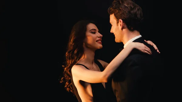 Радісна молода пара дивиться один на одного, танцюючи повільно ізольовано на чорному — стокове фото