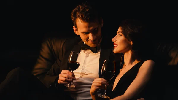 Casal alegre segurando copos de vinho tinto isolado em preto — Fotografia de Stock