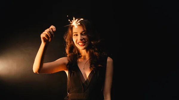 Positivo jovem mulher com sparkler sorrindo no fundo preto — Fotografia de Stock