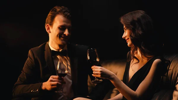 Casal alegre segurando copos de vinho tinto isolado em preto — Fotografia de Stock