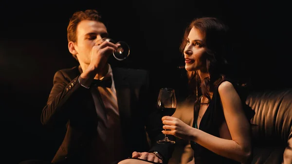 Young woman holding glass while man drinking red wine isolated on black — Stock Photo